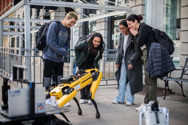 A group of 4 students looking at a yellow robot dog
