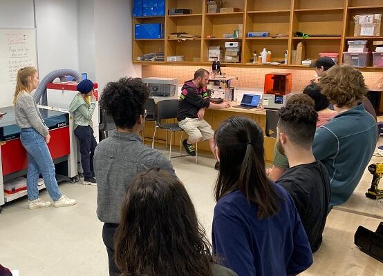 Students learning standing around our 3d printers, while an instuctor shows them how they are used.