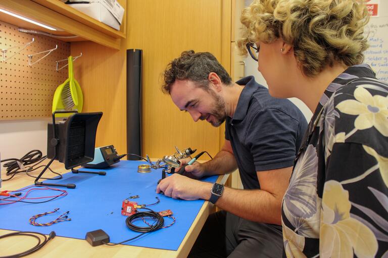 Two students soldering at a work bench in the Assembly workshop