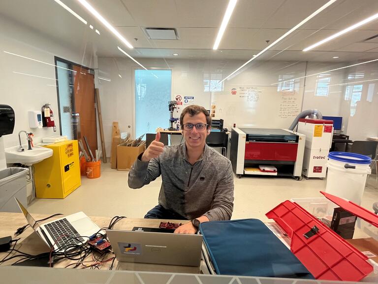 Student giving a thumbs up while working in the workshop with a laptop 