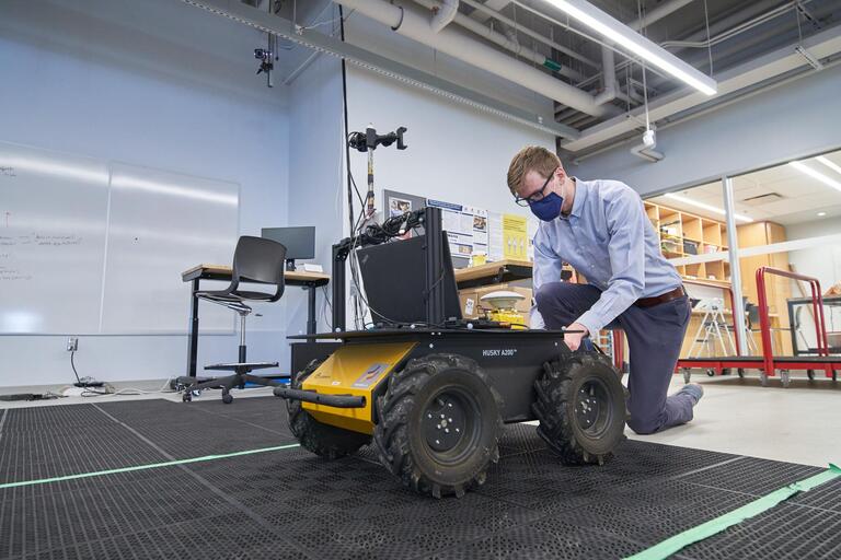 Studnet kneeling down to a Clearpath Husky wheeled robot