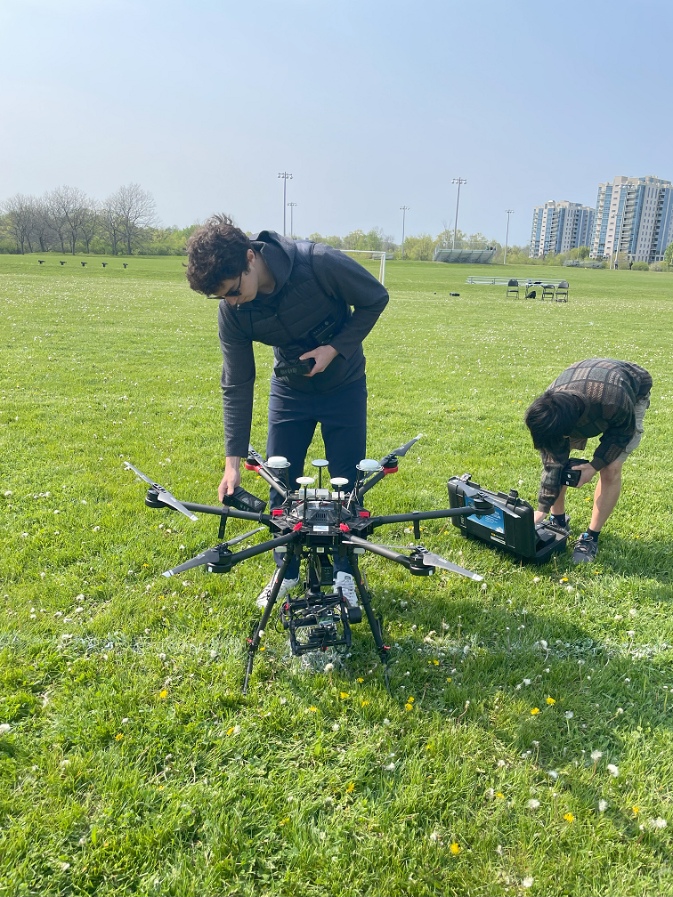 Two students in a field with a large aerial drone getting prepped for flight. 