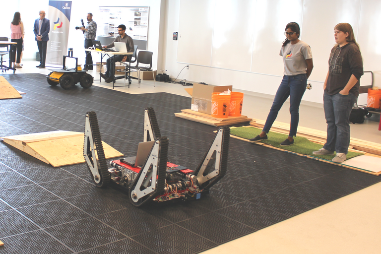 Two students standing next to the Ibex robot, the robot has tracks for wheels. 