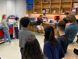 Students learning standing around our 3d printers, while an instuctor shows them how they are used.
