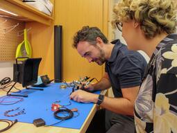 Two students soldering at a work bench in the Assembly workshop