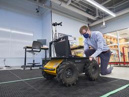 Studnet kneeling down to a Clearpath Husky wheeled robot