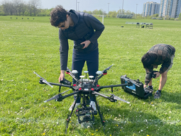 Two students in a field with a large aerial drone getting prepped for flight.